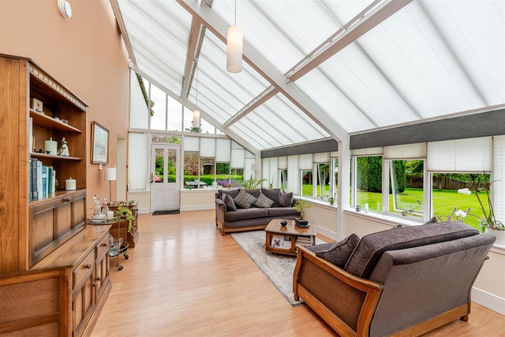 A glass-roofed reception room with sofas and bookcase, windows to the garden